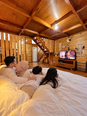 A family of four lying on a bed in a wooden cabin with a television and a staircase. - Miarzafa cabin house (Kejajar)