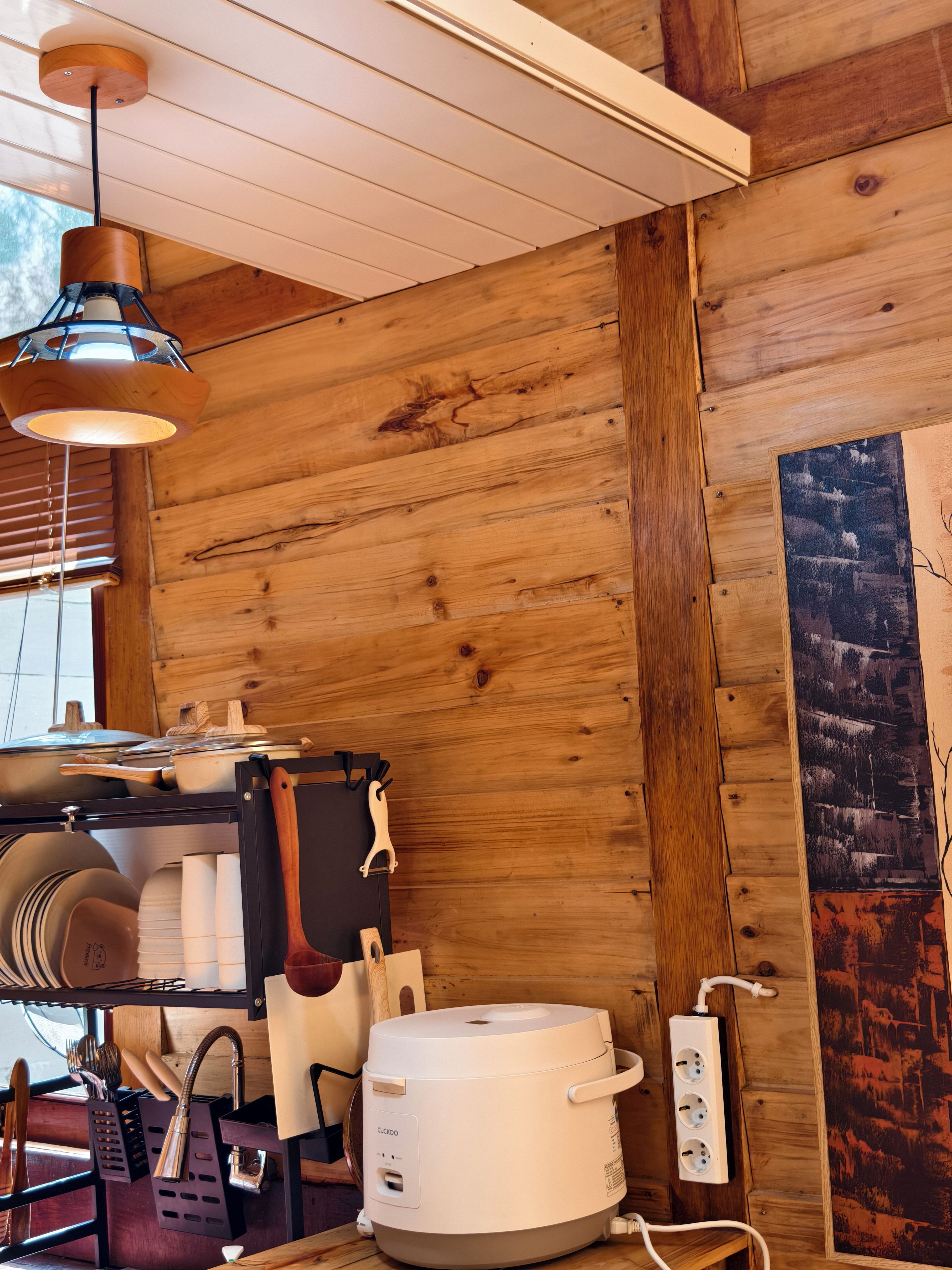 Una cocina con paredes de madera, una lámpara colgante, una encimera con utensilios de cocina y un electrodoméstico blanco.