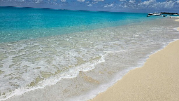 Uma praia com águas turquesa cristalinas, ondas suaves e um areal arenoso.