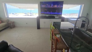 Uma sala de estar com TV, espaço para refeições e vista para a praia.
