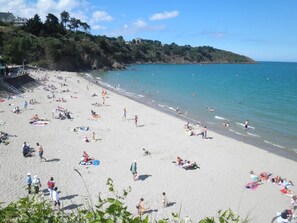 Uma praia com pessoas se banhando ao sol, céu claro e paisagem montanhosa ao fundo.