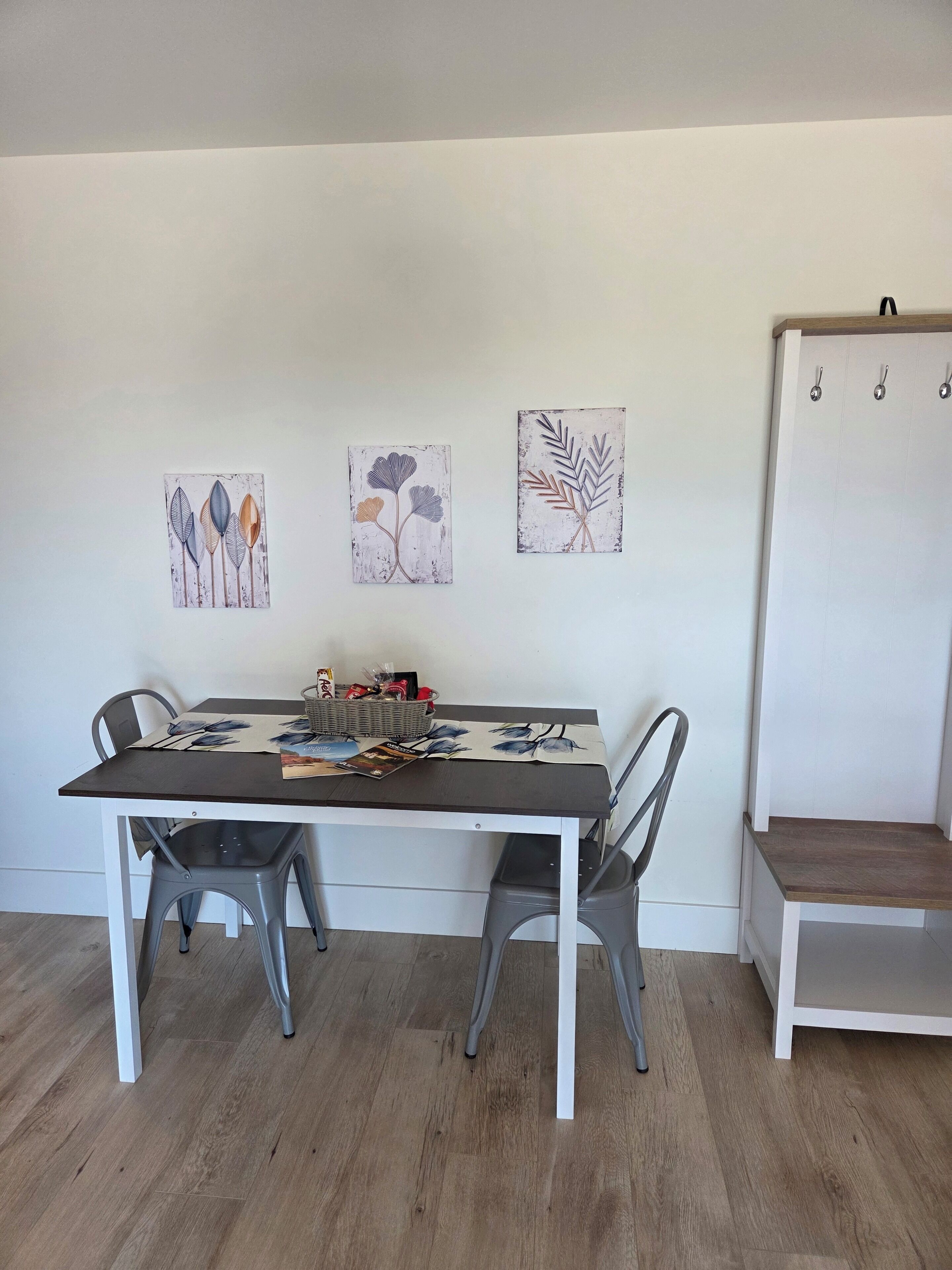 Une table à manger avec des chaises, un panier et un magazine. Deux œuvres d’art sont accrochées au mur au-dessus de la table.
