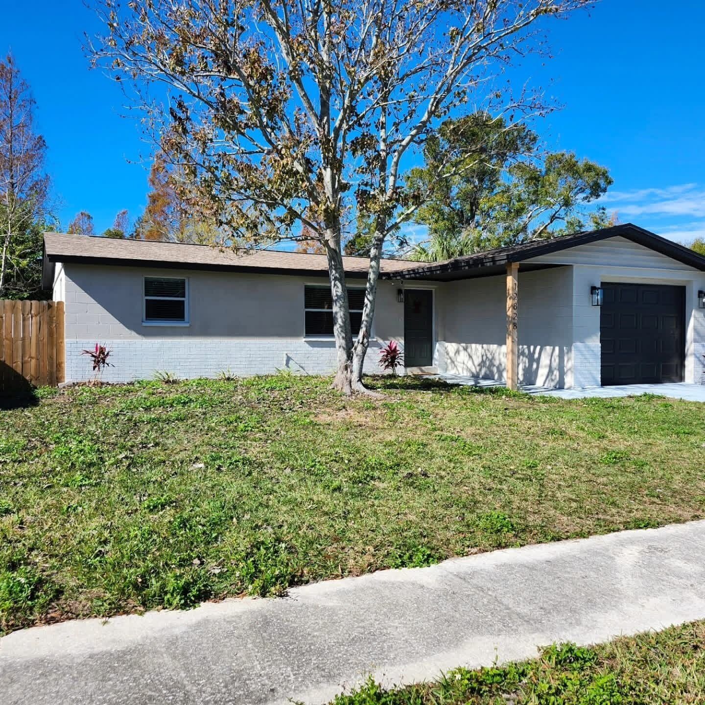 A single-story house with a garage, a small front yard, and a tree.