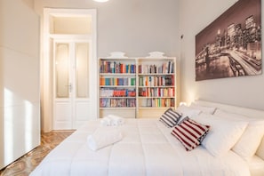 A hotel room with a large bed, a bookshelf, and a cityscape painting.