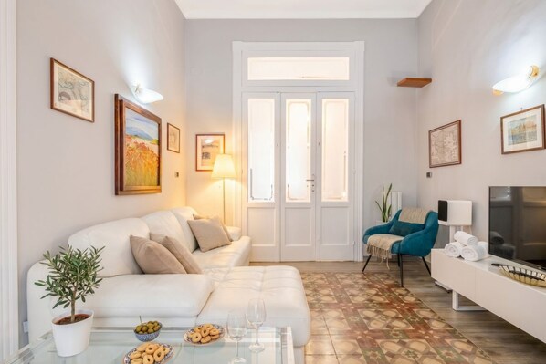 Un salón con sofá, una mesa de centro con aperitivos y vasos, televisor y una puerta con paneles de vidrio.