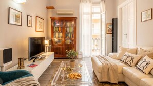 A living room with a sofa, a coffee table with snacks and drinks, a television, and a bookshelf.