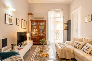 Una sala de estar con un sofá, una mesa de centro con aperitivos y bebidas, un televisor y una estantería.