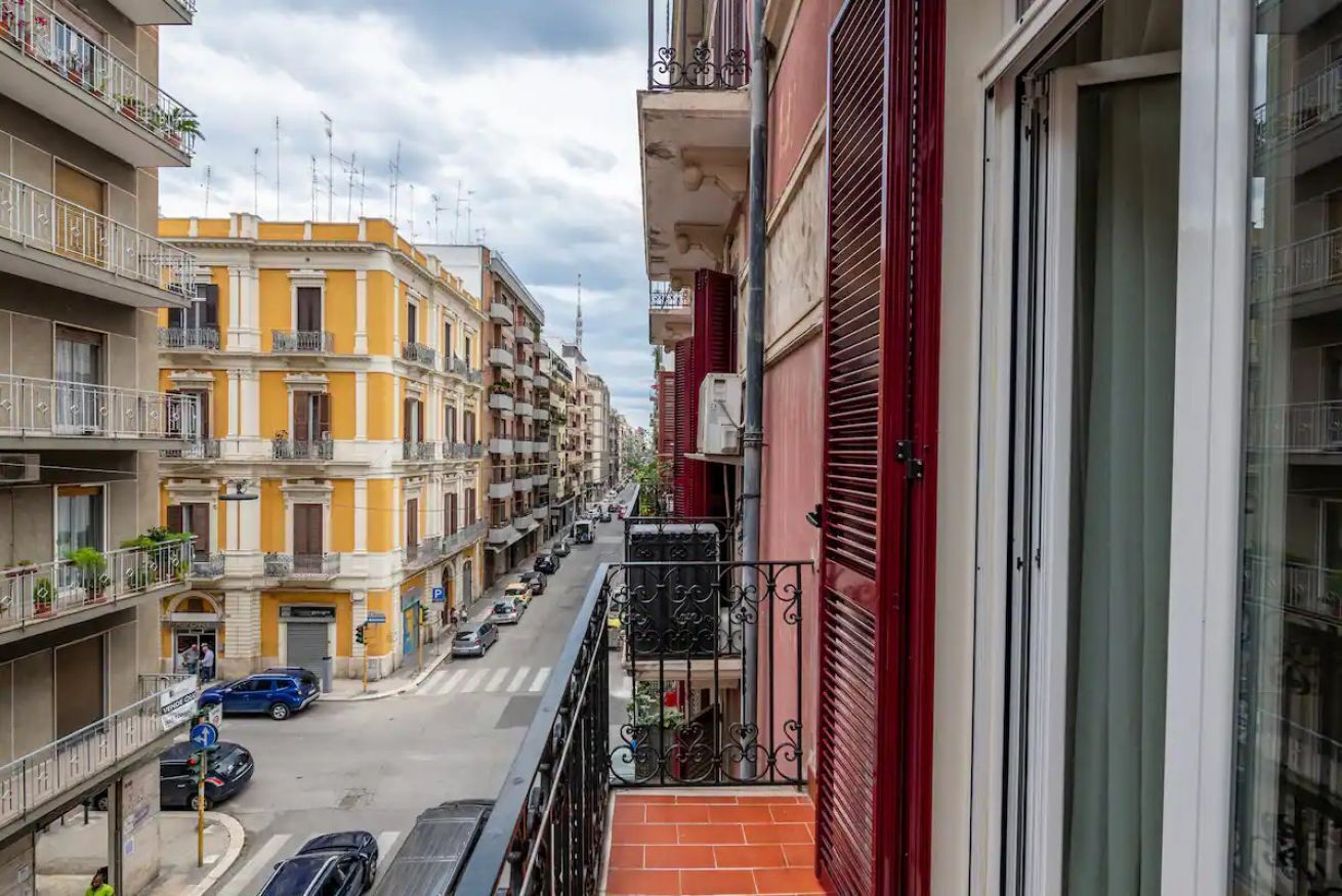 Un immeuble à plusieurs étages, doté de balcons, donnant sur la rue et avec des voitures garées devant.