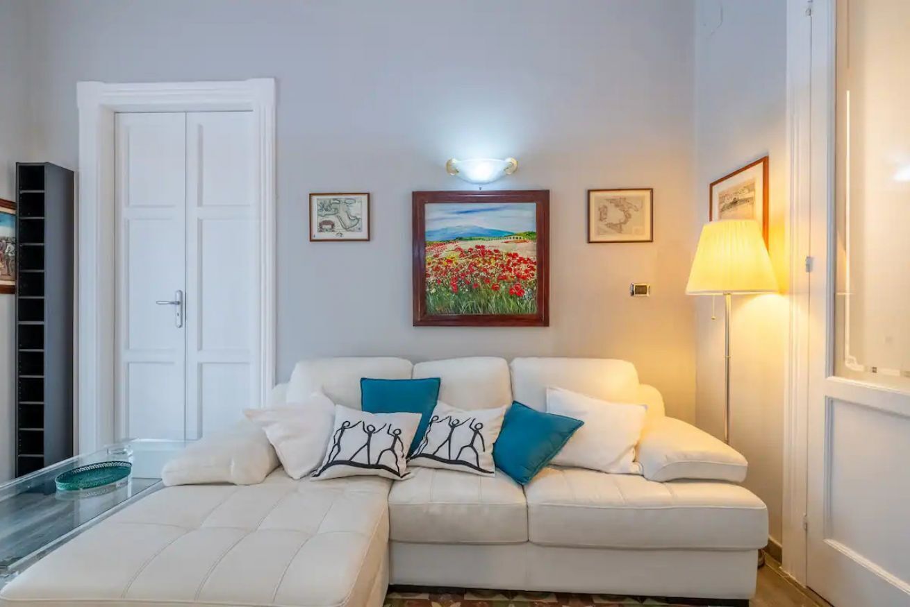 Un salon avec un canapé blanc, une table basse en verre et un tableau représentant des fleurs accroché au mur.