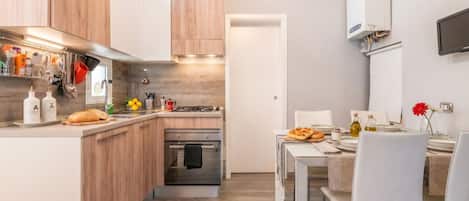 A modern kitchen with wooden cabinets, a built-in oven, and a dining area with a table and chairs.