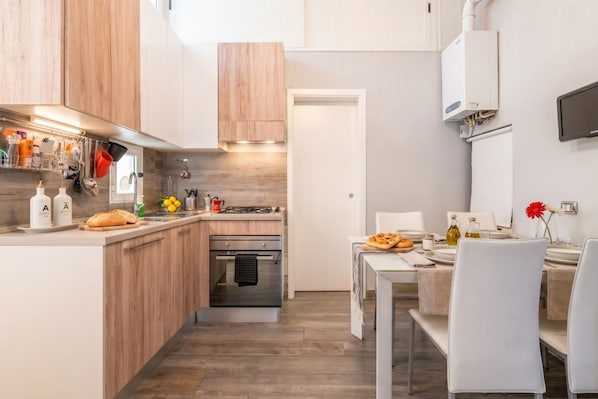 A modern kitchen with wooden cabinets, a built-in oven, and a dining area with a table and chairs.