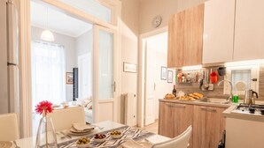 A modern kitchen with wooden cabinets, a dining area with a table set for two, and a view into the adjacent living room.