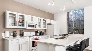Une cuisine moderne avec des meubles blancs, un îlot central doté de tabourets, un four encastré et une grande fenêtre donnant sur la verdure.