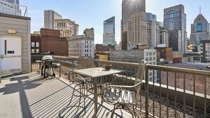 Une terrasse sur le toit, avec une table et des chaises, d’où l’on peut admirer un panorama urbain composé de différents bâtiments.