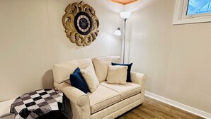 A living room with a beige sofa, a patterned table, a floor lamp, and a decorative wall clock. - Your Clean Clubhouse in St Boniface. Perfect for Students/Short term home away! (Winnipeg)