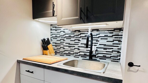 A kitchen with white cabinets, a black backsplash, and a wooden countertop. - Your Clean Clubhouse in St Boniface. Perfect for Students/Short term home away! (Winnipeg)