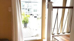 A room with a wooden floor, a white chair, a potted plant, and a view of buildings outside through a window. - Charming Canal Water View Townhome with Outdoor Pool, WiFi & AC in Ocean City (Ocean City)