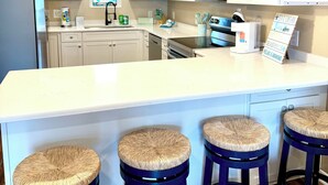 A modern kitchen with white cabinets, a large island with stools, a microwave, and a refrigerator. - Charming Canal Water View Townhome with Outdoor Pool, WiFi & AC in Ocean City (Ocean City)