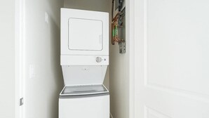 A compact, white laundry room with a built-in washer and dryer, a control panel with visible pipes, and a metal door.