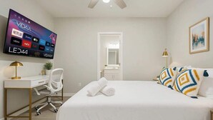 A hotel room with a bed, a desk, a chair, a TV mounted on the wall, and a door leading to the bathroom.