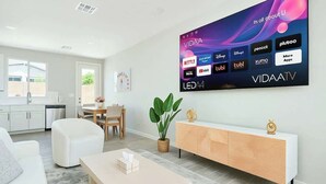 A modern living room with a flat-screen TV displaying various streaming apps, a white sofa, a wooden sideboard, and a coffee table.