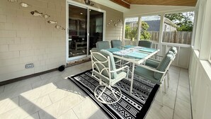 Eine überdachte Terrasse mit Tisch und Stühlen, einem gemusterten Teppich und einer Schiebetür zu einem Raum.