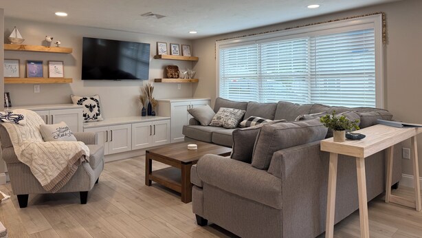 Ein modernes Wohnzimmer mit einer Couch, einem Sessel, einem Couchtisch und einem an der Wand befestigten Fernseher.