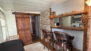 Une pièce chaleureuse avec une porte en bois, un mur en pierre, un coin bar agrémenté d’un miroir et deux fauteuils en cuir.