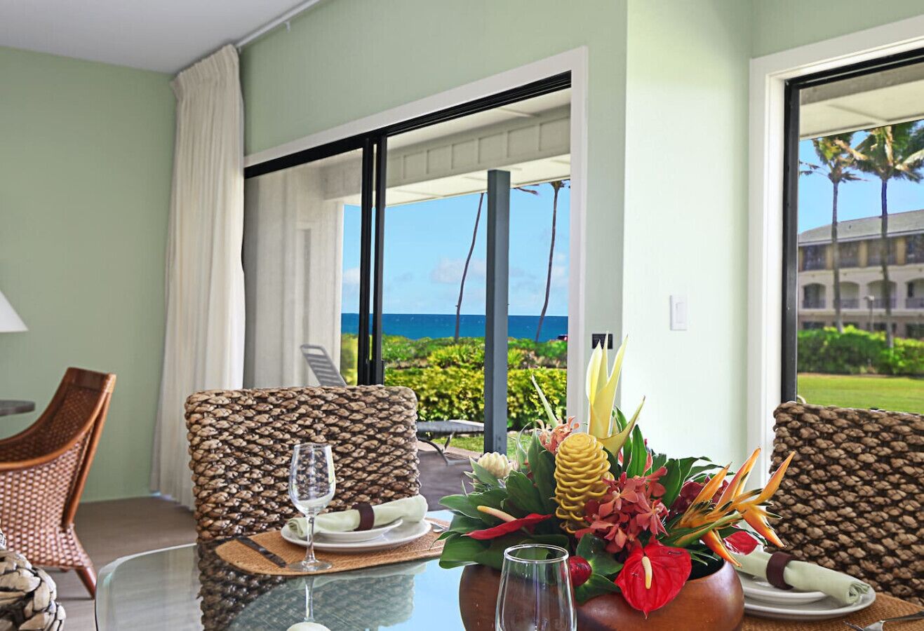 A dining area with wicker chairs, a glass table, and a view of the ocean.