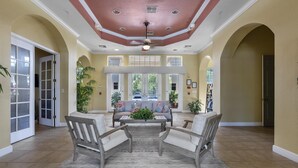 A spacious indoor area with a high ceiling, a central seating area with a table and chairs, and large windows providing natural light. - Trafalgar Resort Community Pool and Gym, Private Pool! (Kissimmee)