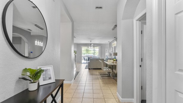 A hallway with a dark console table, a potted plant, and a framed picture. It leads to a dining area with a chandelier and a view of the outdoors. - Trafalgar Resort Community Pool and Gym, Private Pool! (Kissimmee)