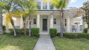 A two-story house with a front porch, a concrete pathway leading to the door, and a small front yard with palm trees and shrubs. - Trafalgar Resort Community Pool and Gym, Private Pool! (Kissimmee)