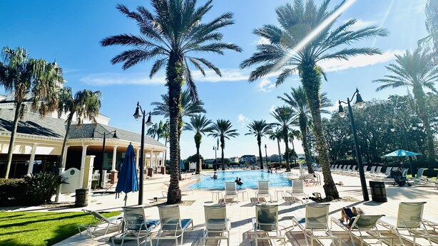 A poolside area with lounge chairs, palm trees, and a building in the background. - Beautiful Condo at Reunion (Kissimmee)