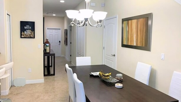 Un coin repas avec une table en bois foncé, des chaises blanches, un lustre et un tableau au mur.