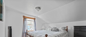 A bedroom with a bed, a nightstand, a lamp, a dresser, and a window with curtains.