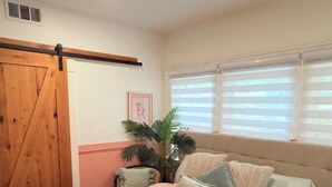 Une chambre à coucher avec un lit, une plante en pot, une fenêtre avec des stores, un luminaire au plafond et une porte coulissante de style rustique.