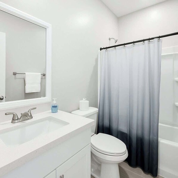 Une salle de bain avec un lavabo blanc, un miroir, des toilettes et un rideau de douche.