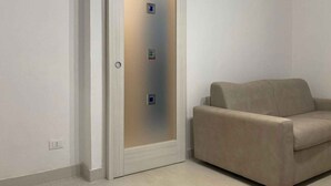 A room with a sliding door, a beige sofa, and a light-colored floor. - Holiday apartment with air conditioning and washing machine (Rosolina Mare)