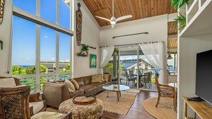 A spacious living room with a large window, a ceiling fan, and a view of the ocean.