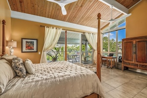 A bedroom with a four-poster bed, a desk with a laptop, and a view of the outdoors.