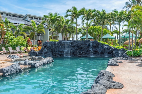 A pool with a waterfall, surrounded by palm trees and lounge chairs.