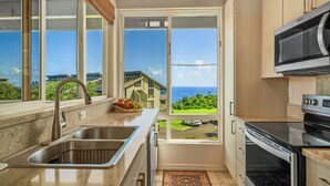 A kitchen with a view of the ocean, a microwave, and a sink.