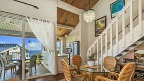 A dining area with wicker chairs, a glass table, and a view of the ocean.