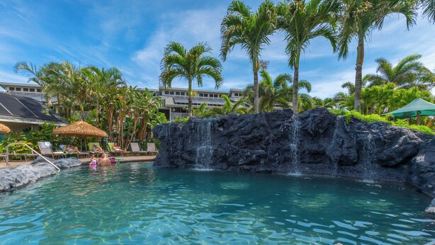 A pool with a waterfall feature, surrounded by palm trees and lounge chairs.