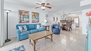 A spacious living room with a blue sofa, wooden coffee table, and a dining area with a blue chair. - Buena Vista 305 | Beachfront | Beach Side Pool in Gulf Shores | My Beach Getaways (Gulf Shores)