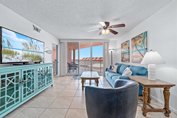 A spacious living room with a television, a blue sofa, a wooden coffee table, and a ceiling fan.