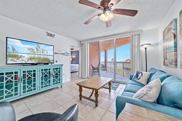 A living room with a TV, teal cabinet, blue sofa, and a ceiling fan. - Buena Vista 305 | Beachfront | Beach Side Pool in Gulf Shores | My Beach Getaways (Gulf Shores)