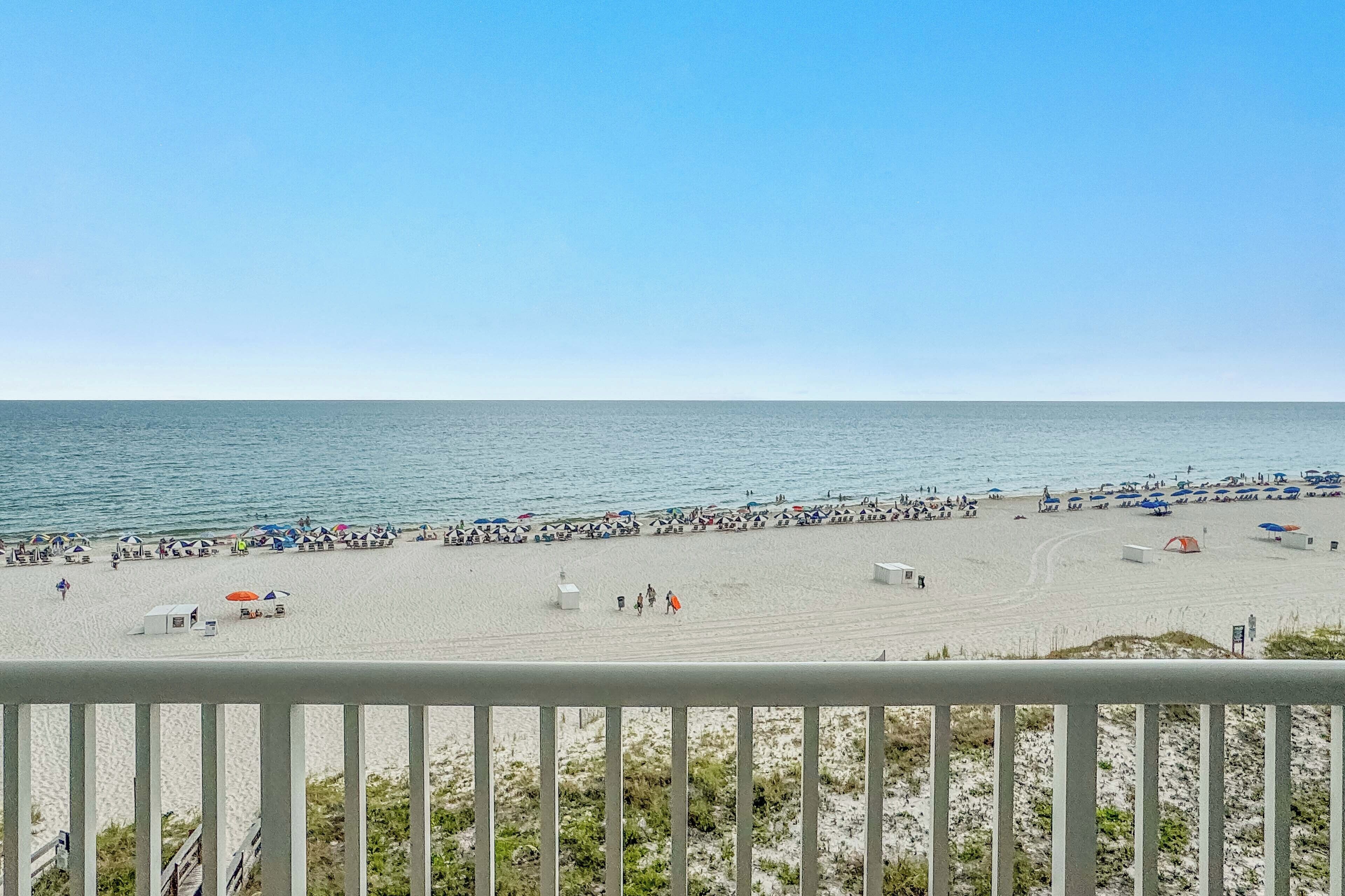 Une plage avec des parasols et des gens, un ciel dégagé et l’océan.