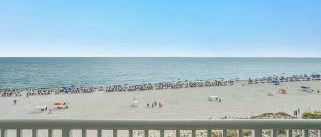 Une plage avec des parasols et des gens, un ciel dégagé et l’océan.