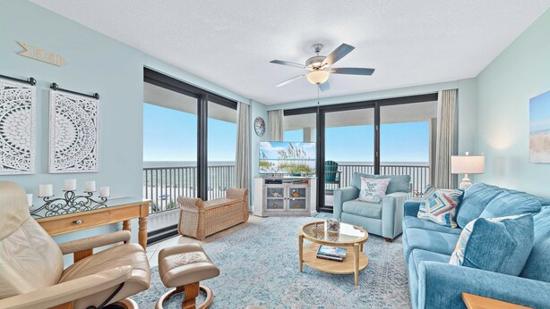 A spacious living room with a large window, a ceiling fan, and a view of the ocean. - Summer House 501B Corner Condo | Oceanfront | Pools, Hot Tub, Tennis | My Beach Getaways (Orange Beach)